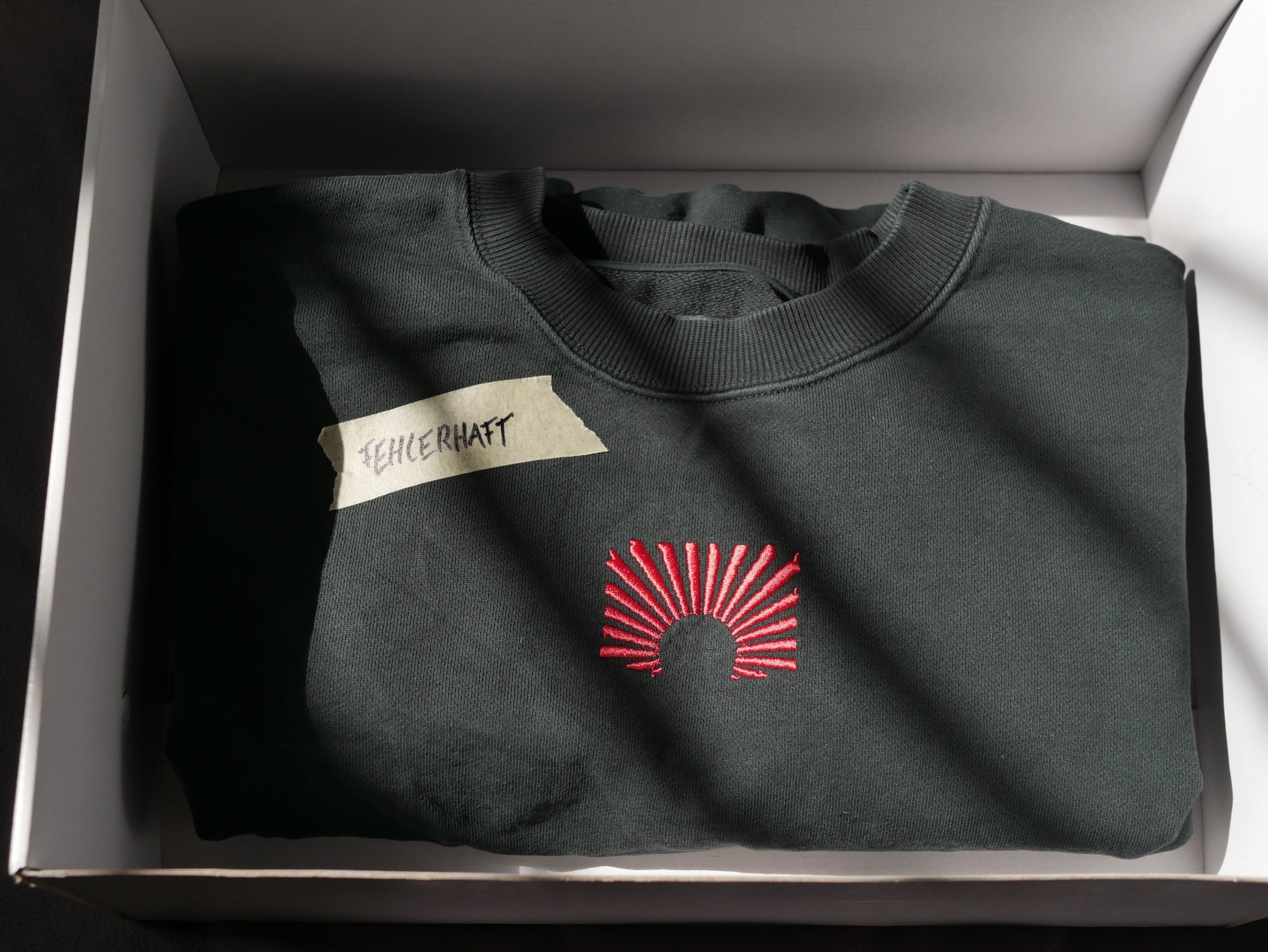 Gefalteter EARLYUP Pullover mit Fehlerhaft-Notiz in einer Box